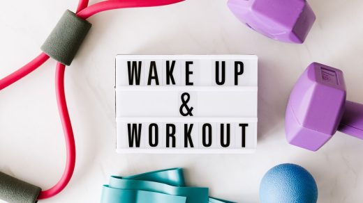 Top view closeup composition of wake up and workout inscription on light box surface among expanders and dumbbells and massag