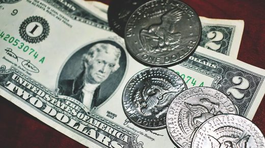 A collection of U.S. currency, including a two-dollar bill and various coins, on a wooden surface.